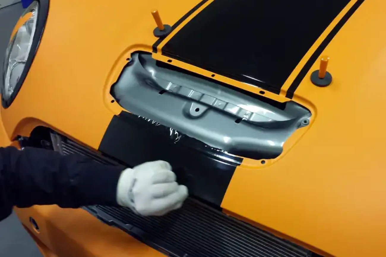 Close-up of matte orange colour change wrap being carefully fitted around bonnet trim on a Mini JCW at Wrap Your Car Kidderminster